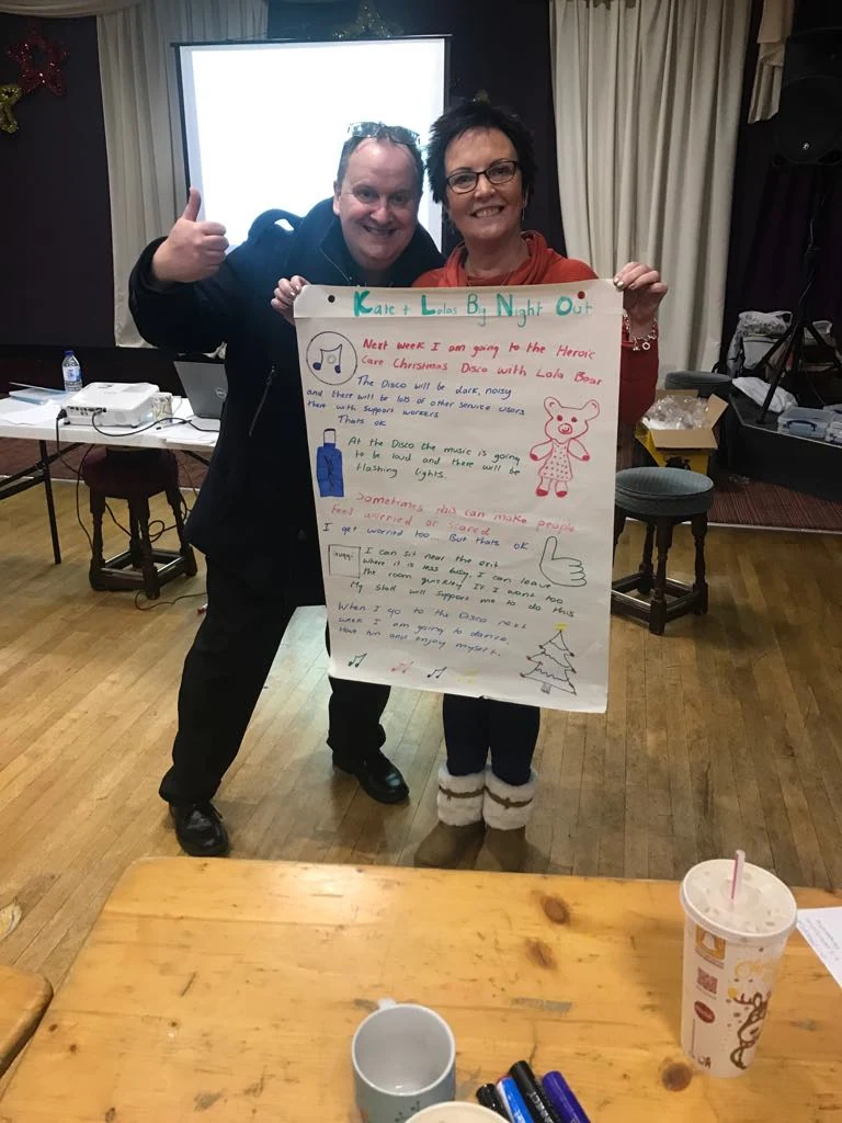 Two people displaying a handwritten activity poster
