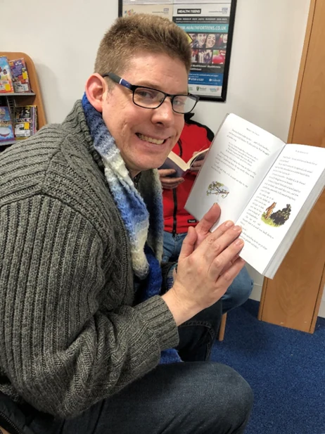 A man smiling while holding an open book