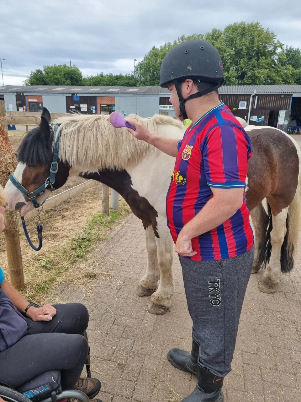 A man wearing a riding helmet beside a pony